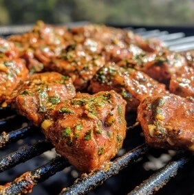 Spiced and marinated chicken pieces grilling on an open flame with visible herbs and spices.